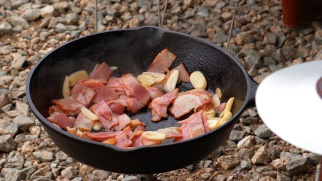 Cooking carrot, garlic and bacon slices in a heated hot frying pan