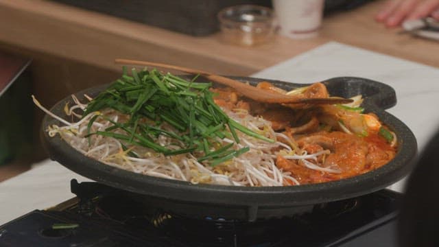 주방에서 숙주나물과 부추가 들어간 매운 제육볶음 요리하기