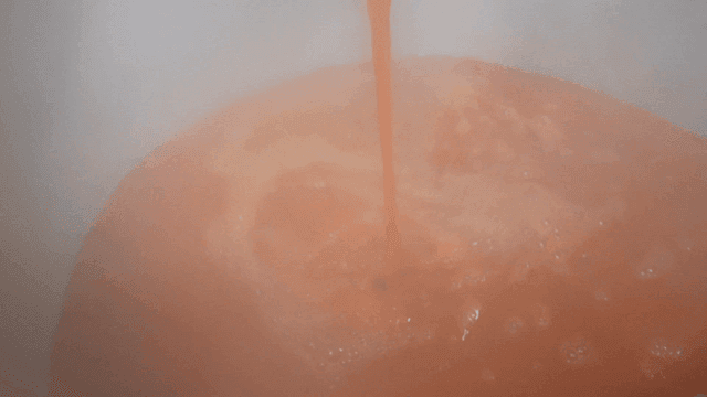 Ladle pouring red broth into large pot