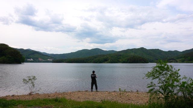 Person fishing by the serene lake on a cloudy day