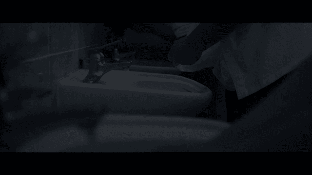 Person washing hands and shirt in dark bathroom