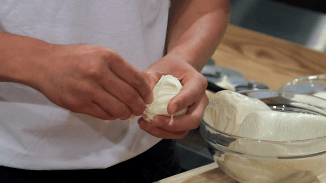Hands putting fresh mozzarella cheese on pizza dough