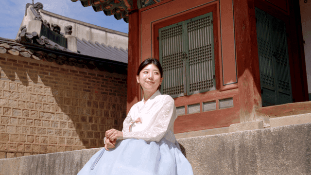 한국 전통 건물 옆에 앉아 있는 한복 입은 여성