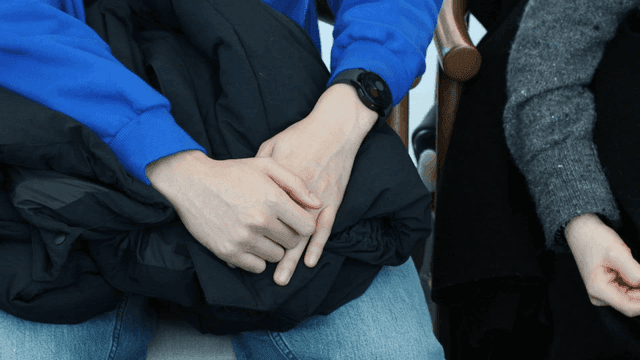 Two people sitting with their hands on top of each other's jackets