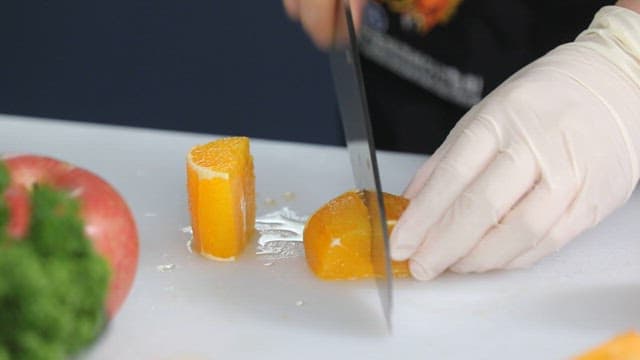 Gloved hand slicing an orange on a cutting board