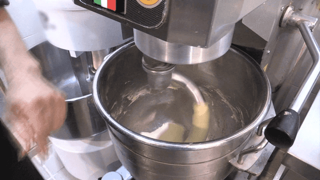 큰 반죽기에 돌아가는 반죽에 버터를 넣는 제빵사