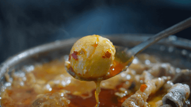Spoon scooping rice cakes from cheese mala hot pot