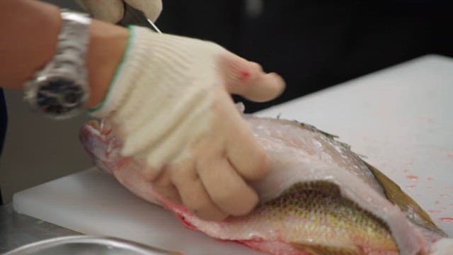 Chef holding a knife in his gloved hand and preparing fish on a kitchen cutting board