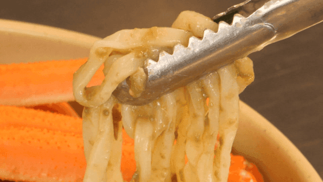Crab noodles being lifted with tongs