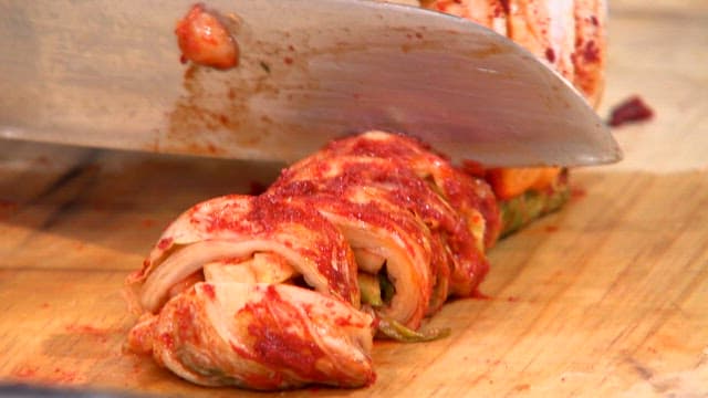 Kimchi being sliced on a wooden board