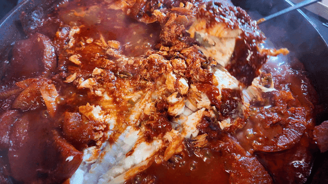 Spoon scooping out spicy braised fish boiling in pot