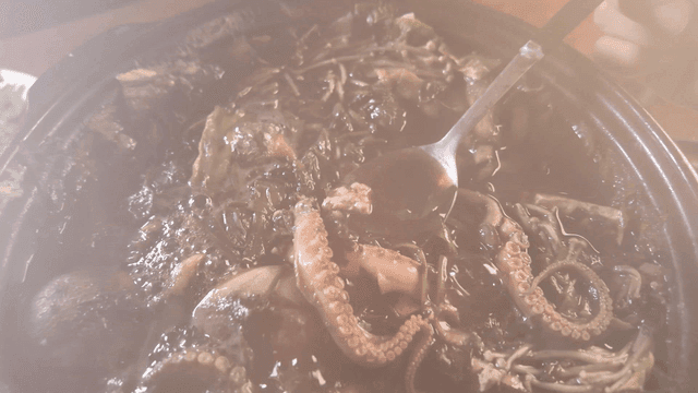 Spoon scooping up hot pot broth containing octopus and vegetables