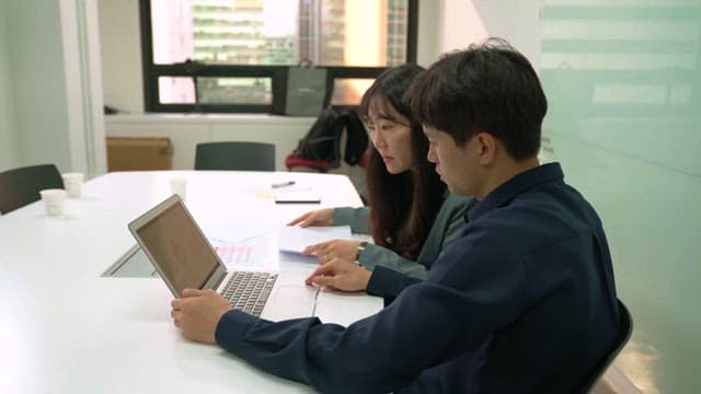 Two people discussing while looking at laptop in office