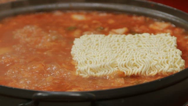 Ramen noodles in kimchi stew boiling in a pot