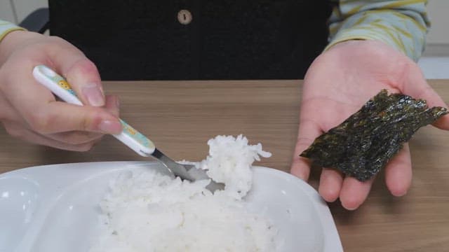 Hands preparing a seaweed wrap with rice