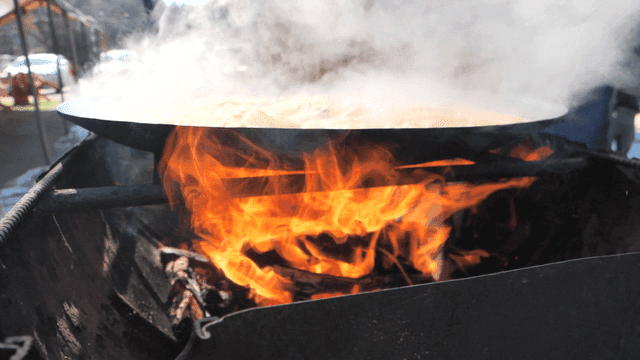 Steaming hot chicken stew in large pot lid over fire