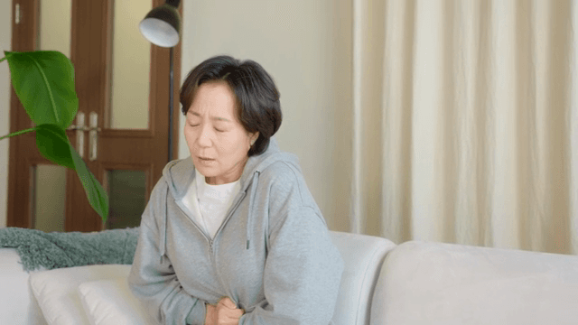 소파에 앉아 배를 잡고 있는 여성