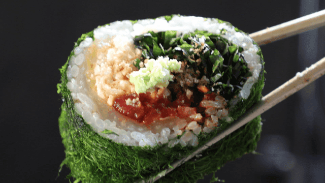 Chopsticks picking up thick aged kimchi and seaweed roll topped with wasabi