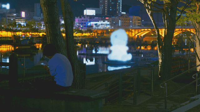 밤에 조형물 불빛이 비치는 강가 벤치의 사람