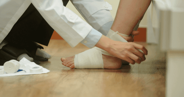 환자의 발목에 붕대를 감고 있는 의사