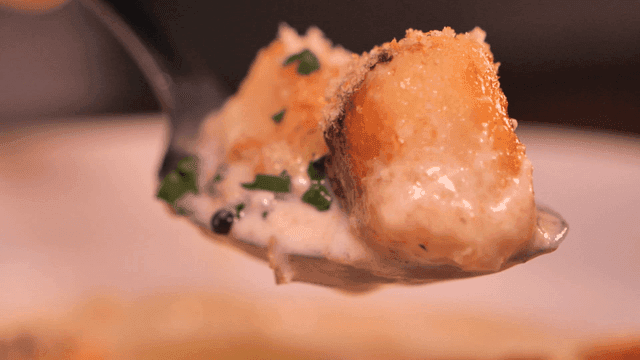 Scene of spooning creamy gnocchi with herbs