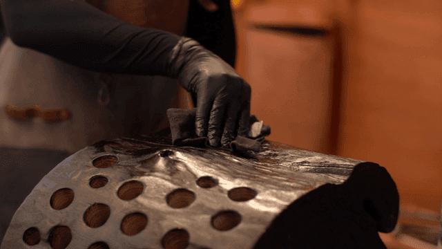 Artisan applying oil to dark wooden sculpture
