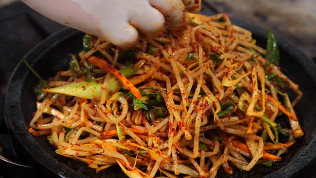 Seasoned bean sprouts being placed on a grill