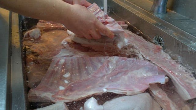 Washing large cuts of raw meat under running water in a kitchen