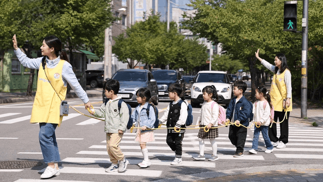 Kindergarten children crossing road with their teacher