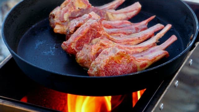 Fresh lamb being cooked in a frying pan on the portable stove