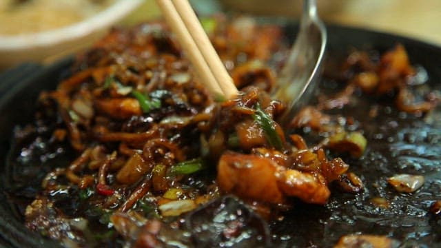 Chopstickful of seafood Jjajang noodles on an iron plate with steaming hot sauce