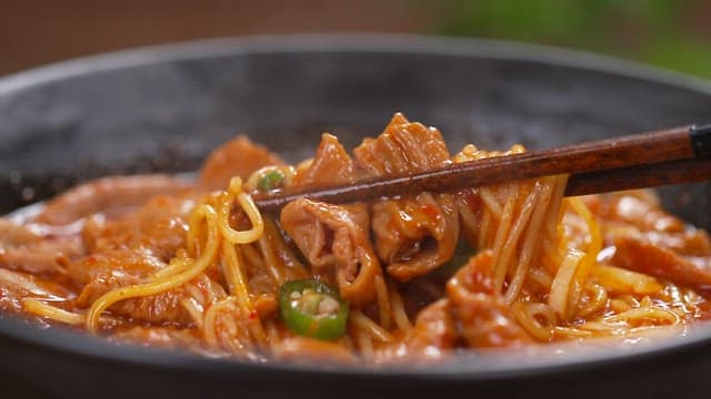 Chopstickful of spicy seasoned noodles with steam rising from the bowl