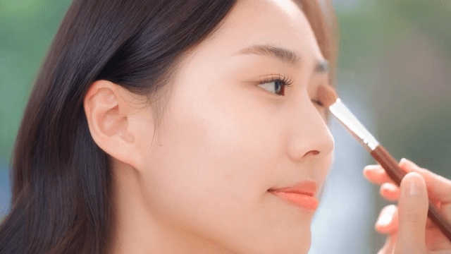 밝게 빛나는 방에서 브러쉬를 이용해 눈화장을 하고있는 여성