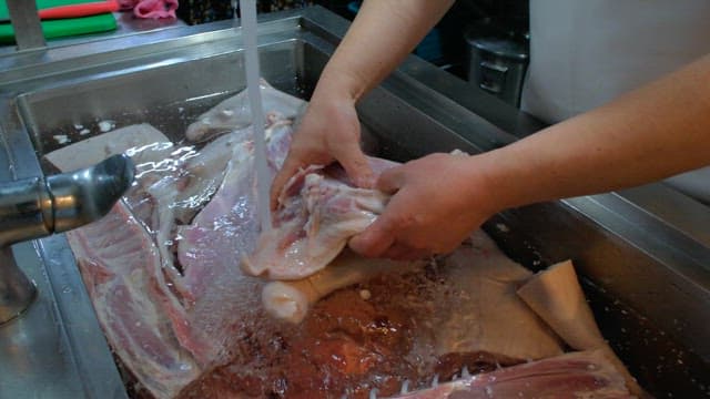 Washing large cuts of raw meat under running water in a kitchen