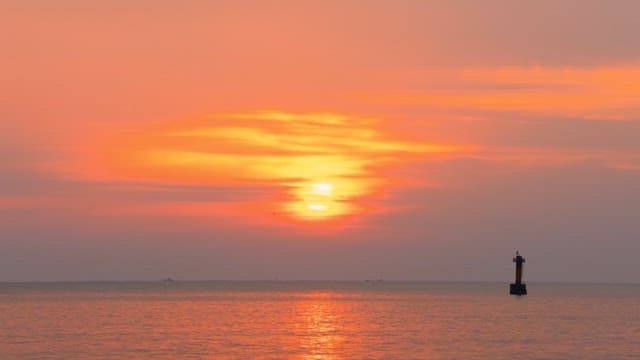 Red sunset coloring the calm and peaceful sea and lighthouse