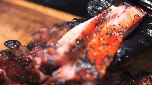 Gloves on hands removing bones from Texas barbecue ribs