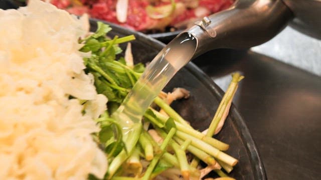 전골 요리를 위해 신선한 채소와 버섯에 육수를 붓는 장면