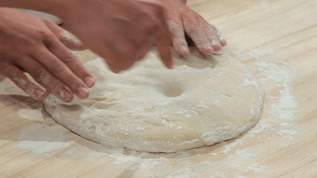 Hands pressing dough on a cutting board