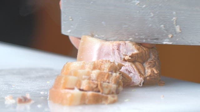 부엌에서 도마 위에 조리된 돼지고기 수육을 칼로 자르기