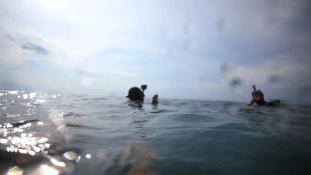 Scuba divers floating on the ocean surface under cloudy sky