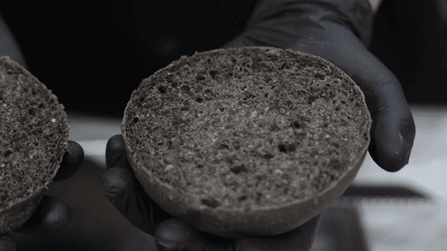 Black burger bun held with gloves