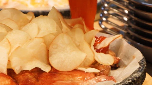 Pouring hot sauce over pizza with potato chips