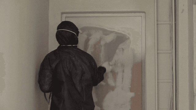 Worker spraying paint on a door in a narrow hallway