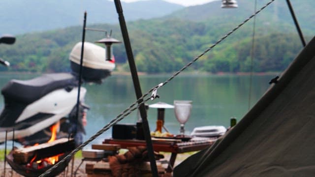 Camping by a serene lakeside with a tent, campfire, and a motorcycle