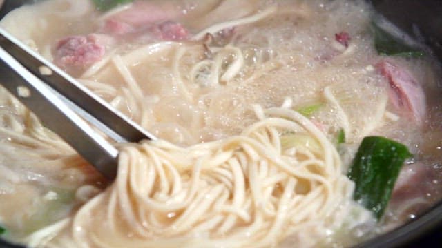 Noodles picked from the noodle soup with chicken boiling in the pot