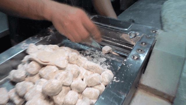 주방에서 만두피 펴내는 기계에 반죽을 계속 넣는 손