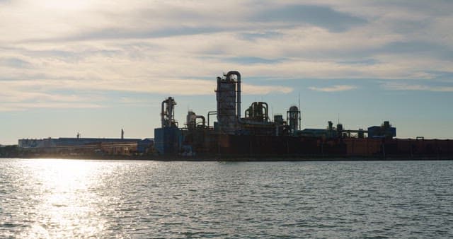 저녁의 노을지는 하늘 아래 바다 근처에 위치한 산업 공장