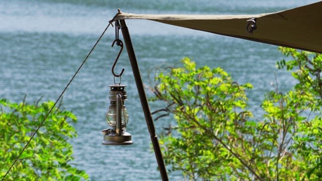 Lantern hangs under a tarp by a lake surrounded by greenery.