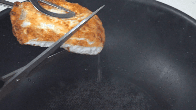Fried egg over a hot oil pan being cut by scissors