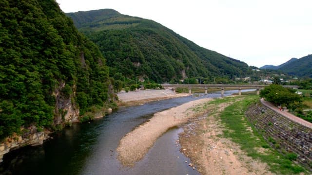 Scenic view of river flowing under a distinctive curved bridge in a mountainous area